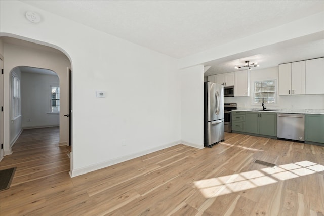 kitchen with green cabinetry, light wood-style flooring, a sink, white cabinets, and appliances with stainless steel finishes