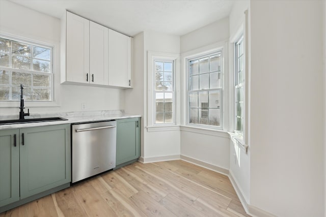 kitchen featuring a sink, light countertops, light wood-style flooring, stainless steel dishwasher, and green cabinetry