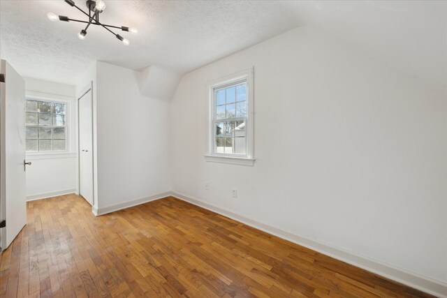 additional living space featuring lofted ceiling, hardwood / wood-style floors, and a textured ceiling