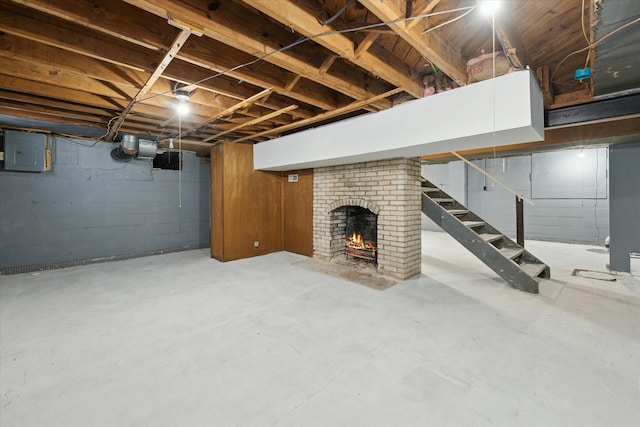 unfinished below grade area with a brick fireplace, stairway, and electric panel