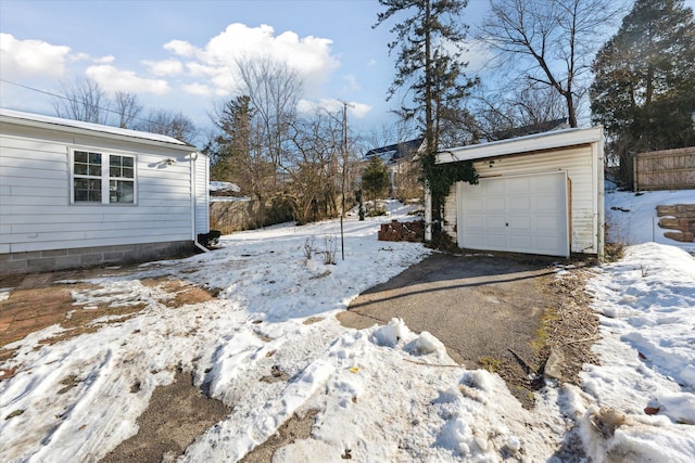 yard layered in snow featuring an outbuilding, aphalt driveway, a garage, and fence