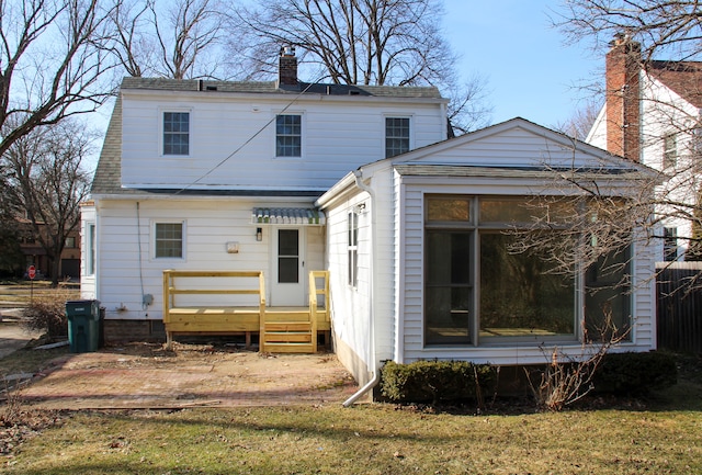 rear view of property with a lawn, a chimney, roof with shingles, and a sunroom