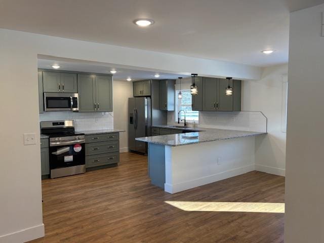 kitchen with dark wood-type flooring, sink, appliances with stainless steel finishes, kitchen peninsula, and backsplash