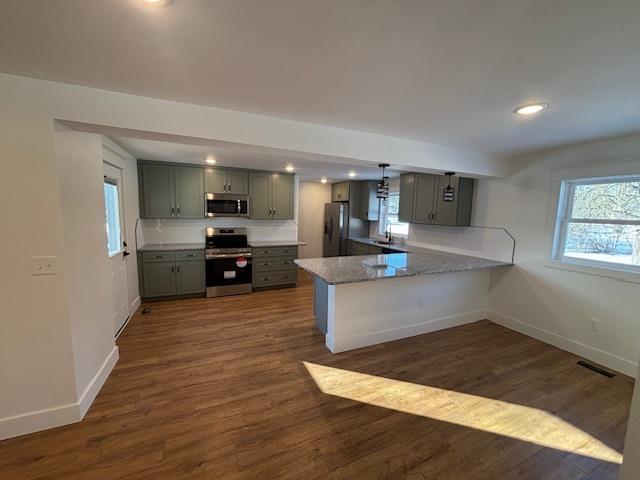 kitchen featuring sink, appliances with stainless steel finishes, light stone countertops, dark hardwood / wood-style flooring, and kitchen peninsula