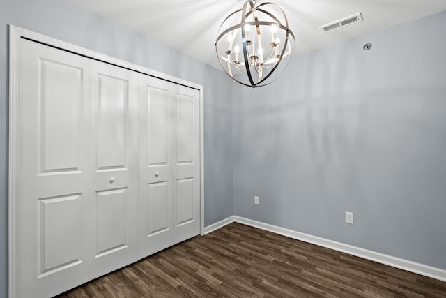 unfurnished bedroom with dark hardwood / wood-style flooring, a closet, and a chandelier