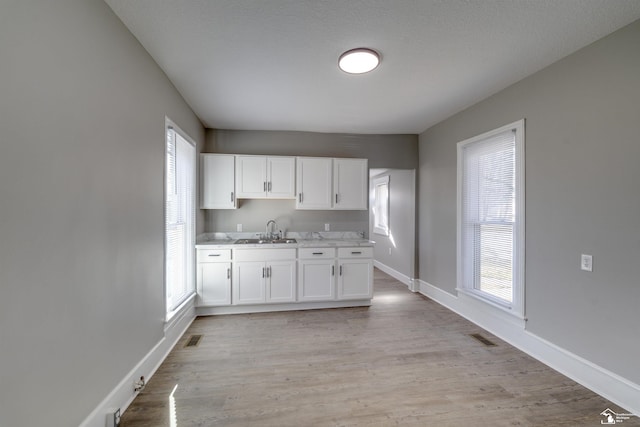 kitchen with white cabinetry, sink, a textured ceiling, and light hardwood / wood-style floors