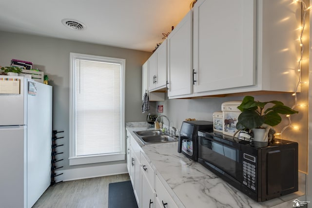 kitchen with light stone counters, sink, white cabinets, and white fridge