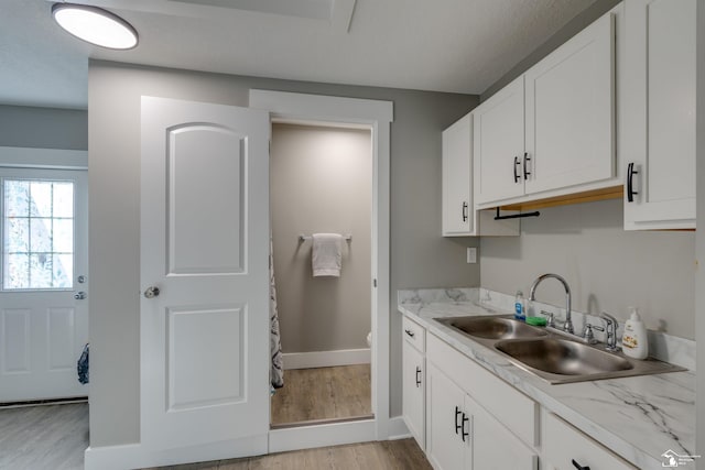 interior space with light stone counters, sink, white cabinets, and light wood-type flooring