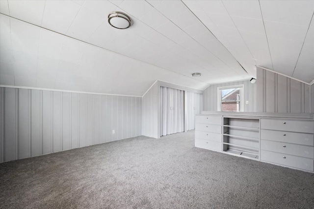 bonus room featuring lofted ceiling, carpet, and wood walls