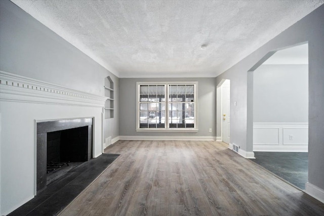 unfurnished living room featuring built in shelves, dark hardwood / wood-style floors, and a textured ceiling