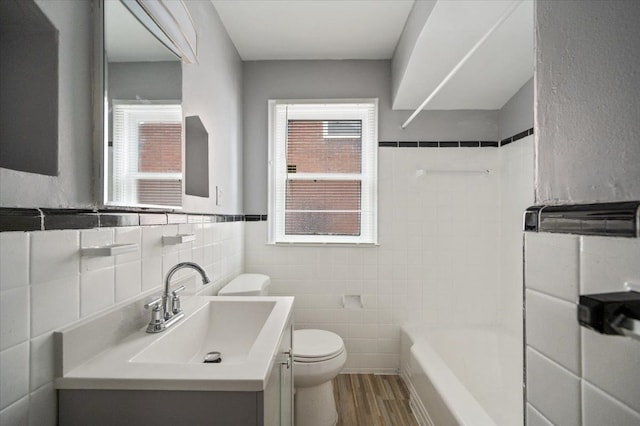 full bathroom with shower / washtub combination, wood-type flooring, tile walls, vanity, and toilet