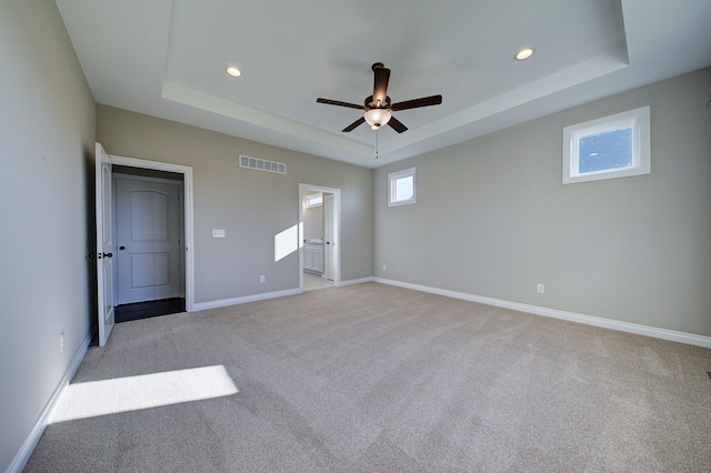 unfurnished bedroom featuring visible vents, a raised ceiling, and light colored carpet