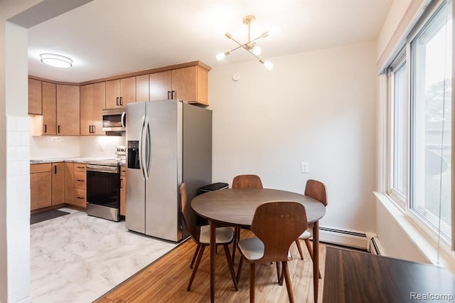 kitchen with light brown cabinetry, tasteful backsplash, a chandelier, baseboard heating, and stainless steel appliances