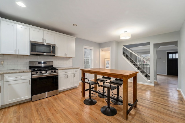 kitchen featuring backsplash, light wood-type flooring, white cabinets, and appliances with stainless steel finishes