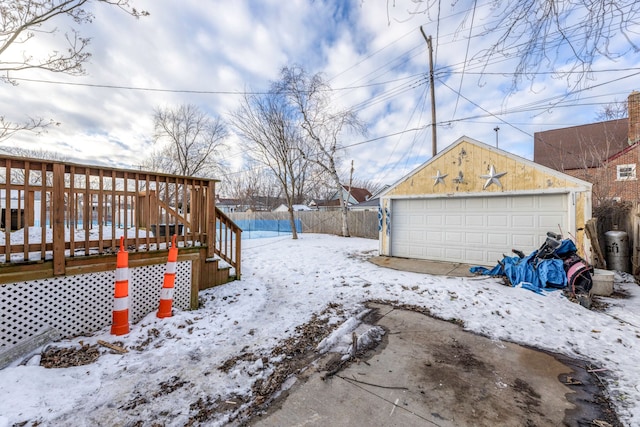 yard covered in snow featuring a garage, a wooden deck, and an outbuilding