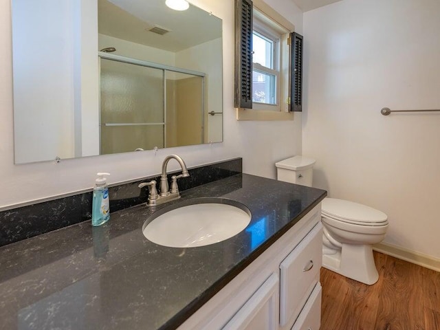 bathroom with wood-type flooring, toilet, a shower with shower door, and vanity