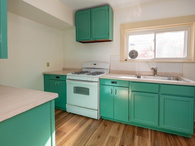 kitchen with sink, white range with gas stovetop, green cabinets, backsplash, and light hardwood / wood-style floors