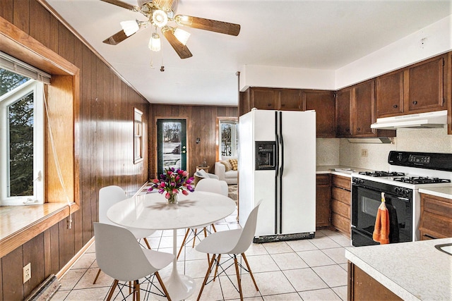 kitchen featuring range with gas cooktop, wood walls, tasteful backsplash, white refrigerator with ice dispenser, and light tile patterned floors