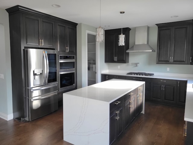 kitchen featuring wall chimney range hood, appliances with stainless steel finishes, hanging light fixtures, a kitchen island, and dark hardwood / wood-style flooring