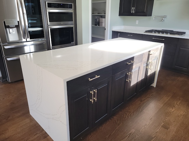 kitchen featuring stainless steel appliances, light stone countertops, a center island, and dark wood-type flooring