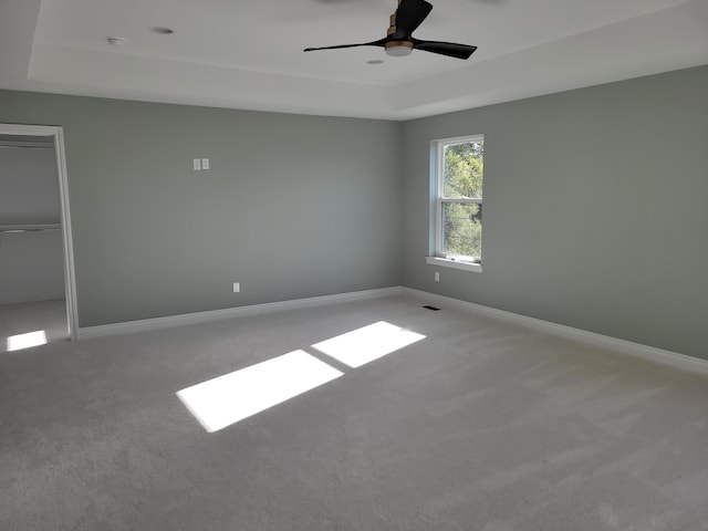 empty room with carpet flooring, ceiling fan, and a tray ceiling