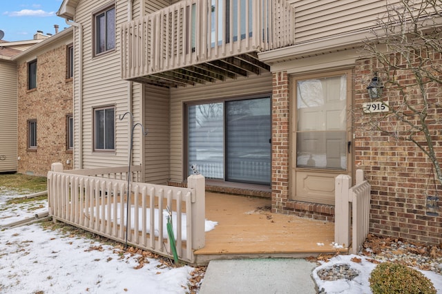 snow covered property entrance featuring a balcony and a deck