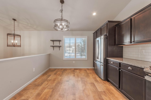 kitchen featuring stainless steel refrigerator, decorative light fixtures, tasteful backsplash, light stone countertops, and dark brown cabinets