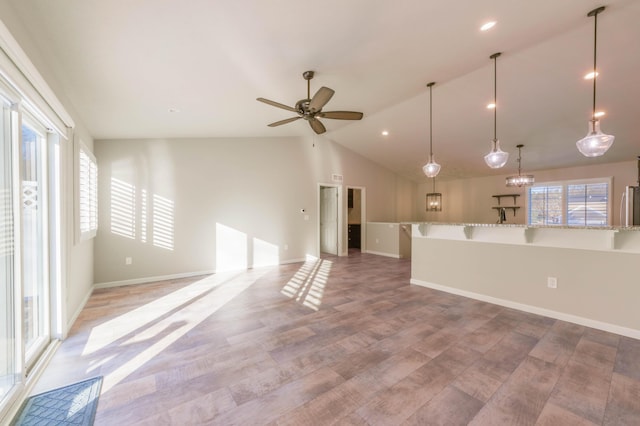 unfurnished living room with vaulted ceiling, ceiling fan with notable chandelier, and light hardwood / wood-style flooring