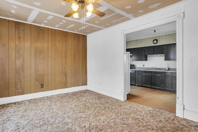 unfurnished living room with ceiling fan, sink, and wooden walls