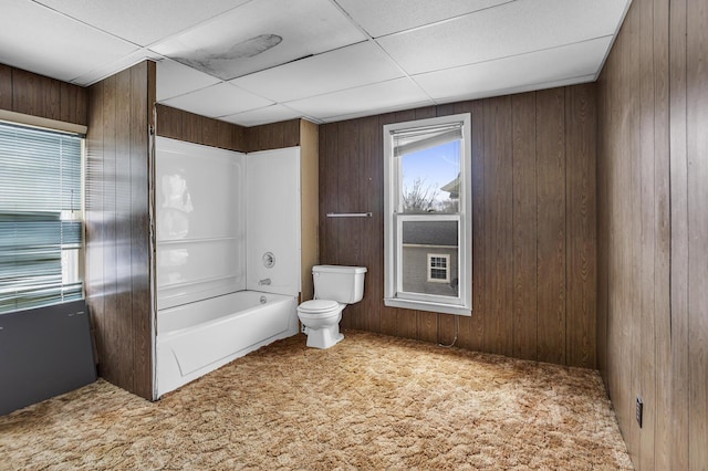 bathroom with shower / bathing tub combination, a paneled ceiling, toilet, and wood walls