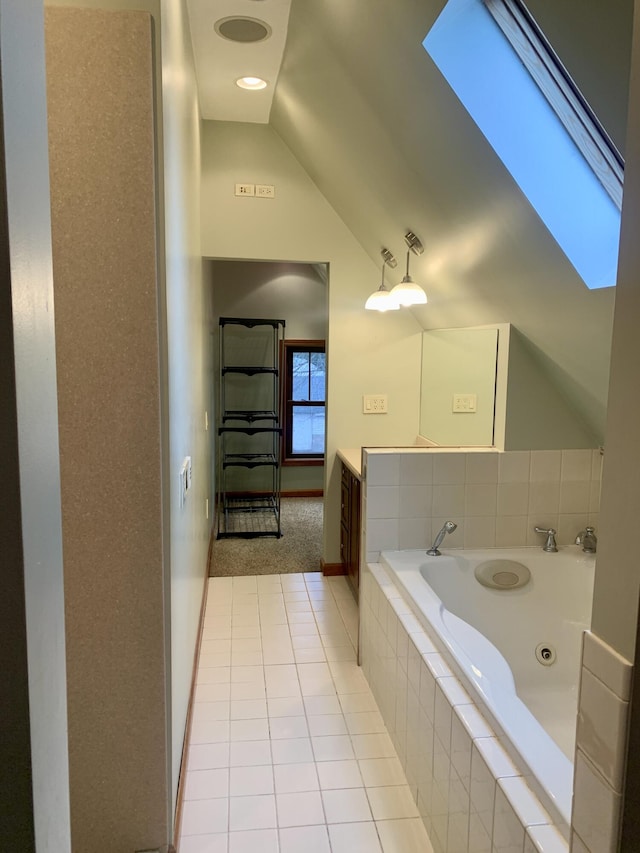 bathroom featuring tile patterned flooring, lofted ceiling with skylight, tiled tub, and vanity