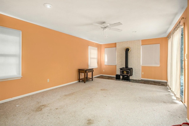 unfurnished living room featuring carpet, a wood stove, and ceiling fan