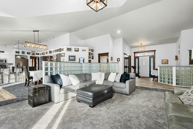 living room with lofted ceiling, track lighting, a chandelier, and carpet flooring