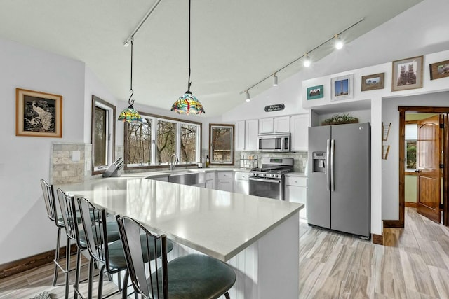 kitchen featuring white cabinetry, backsplash, stainless steel appliances, a kitchen bar, and decorative light fixtures