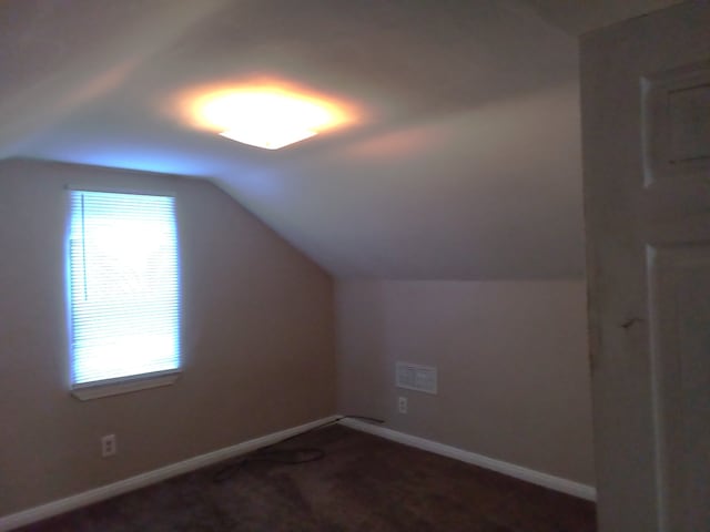 additional living space featuring lofted ceiling and dark carpet