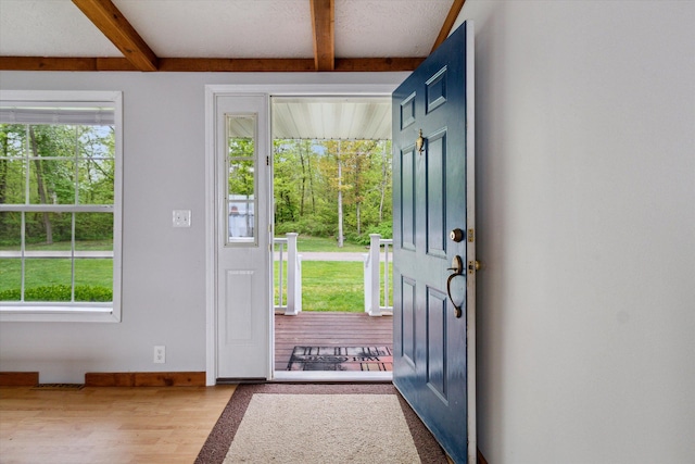 doorway to outside featuring hardwood / wood-style floors, beam ceiling, and a textured ceiling