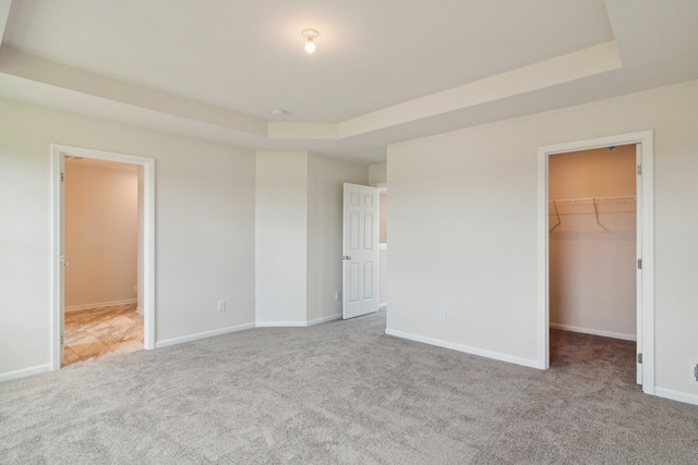 unfurnished bedroom with a spacious closet, light colored carpet, a raised ceiling, ensuite bath, and a closet