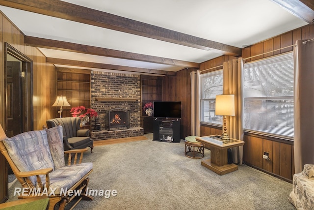 living area featuring carpet flooring, wooden walls, a brick fireplace, and beam ceiling