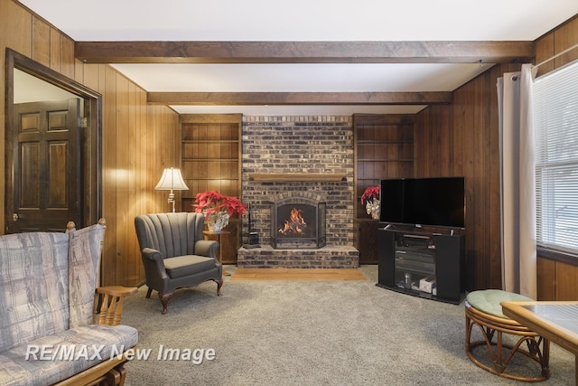 living area featuring beamed ceiling, a brick fireplace, carpet flooring, and wooden walls