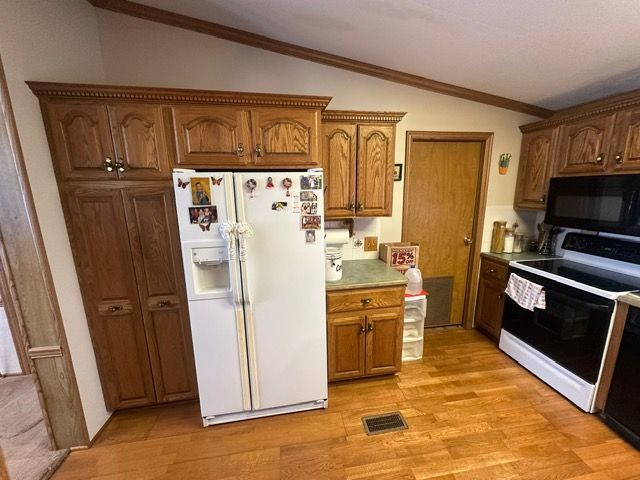 kitchen featuring range with electric stovetop, vaulted ceiling, white fridge with ice dispenser, and light wood-type flooring