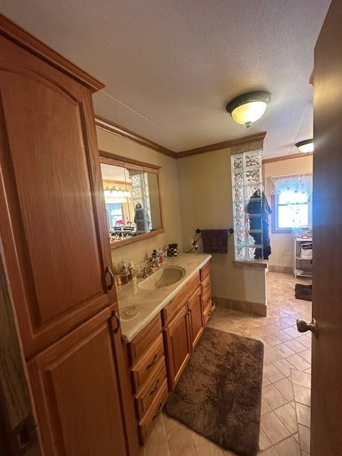 bathroom featuring tile patterned flooring, crown molding, vanity, and a textured ceiling