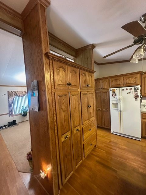 kitchen with crown molding, light hardwood / wood-style floors, white fridge with ice dispenser, and ceiling fan