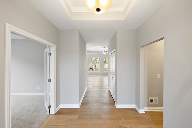 hall featuring crown molding, light hardwood / wood-style floors, and a tray ceiling