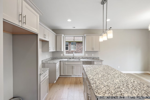 kitchen with sink, a center island, light hardwood / wood-style flooring, pendant lighting, and light stone countertops