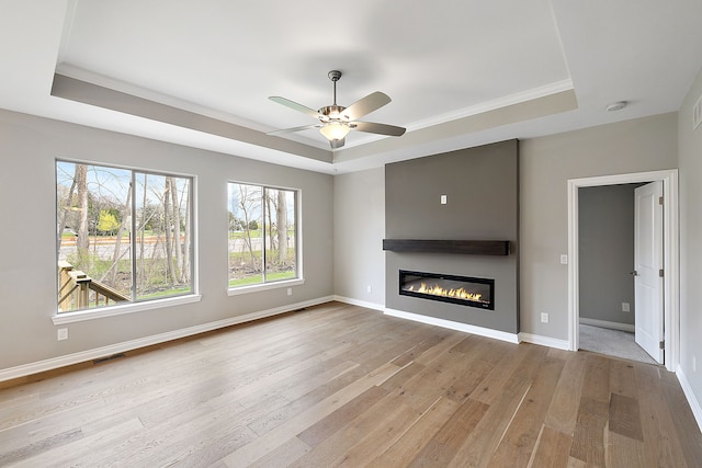 unfurnished living room with ceiling fan, a fireplace, light hardwood / wood-style floors, and a tray ceiling