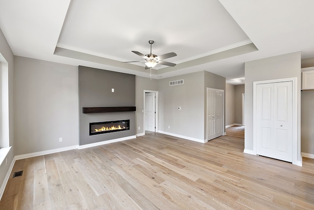 unfurnished living room featuring ceiling fan, a tray ceiling, and light hardwood / wood-style floors