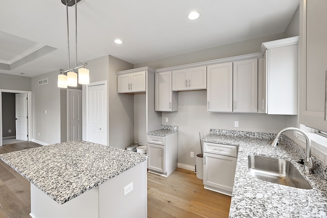 kitchen featuring a kitchen island, sink, white cabinets, light stone counters, and light wood-type flooring