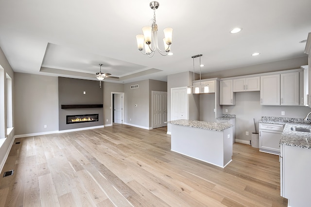 kitchen with sink, hanging light fixtures, a center island, a tray ceiling, and light stone countertops