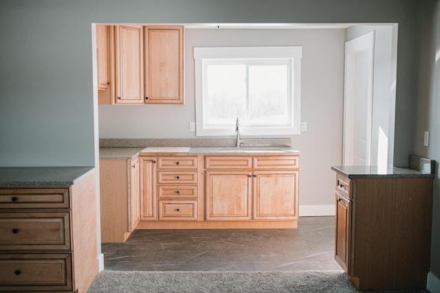 kitchen with light brown cabinetry, baseboards, and a sink