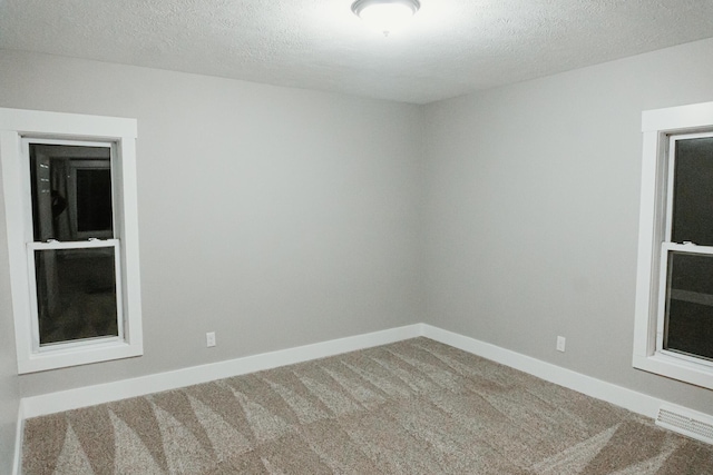 empty room featuring visible vents, baseboards, a textured ceiling, and carpet flooring